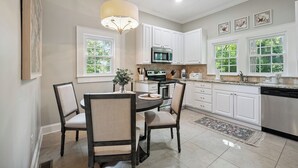 A modern kitchen with white cabinets, a central island, and a dining area with chairs. - Bluebird Cottage in heart of Hickory, NC (Hickory)