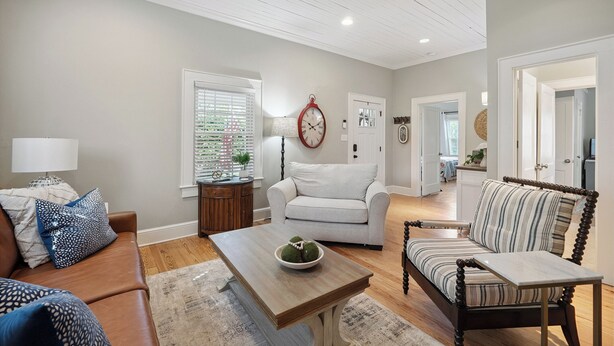 A living room with a sofa, armchair, coffee table, and a clock on the wall. - Bluebird Cottage in heart of Hickory, NC (Hickory)