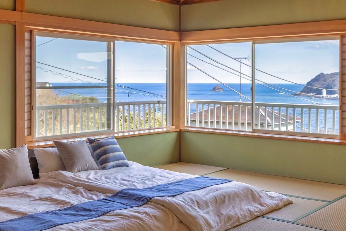 A room with a bed, a view of the sea, and a balcony.