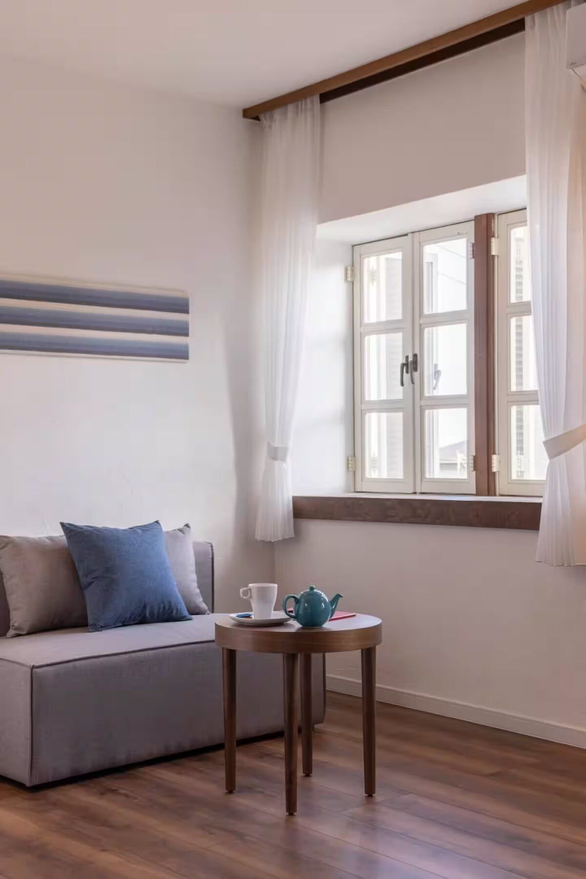 A room with a sofa, a small round table with a cup and a teapot, and a window with curtains.