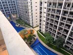 Un immeuble de grande hauteur doté de nombreux balcons, une cour intérieure avec une piscine et de nombreux espaces verts environnants.