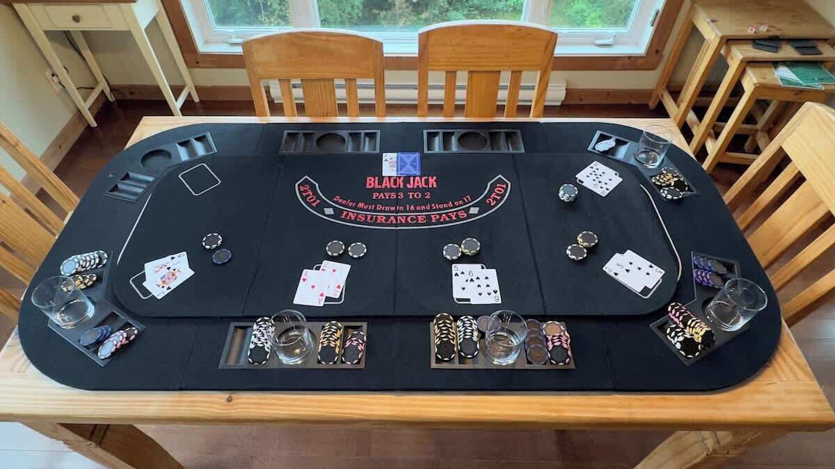 A blackjack table with cards and chips, set in a room with wooden furniture and a window.