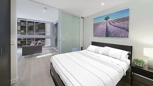 Une chambre moderne avec un grand lit, une porte vitrée donnant sur un balcon et un tableau représentant des champs de lavande.