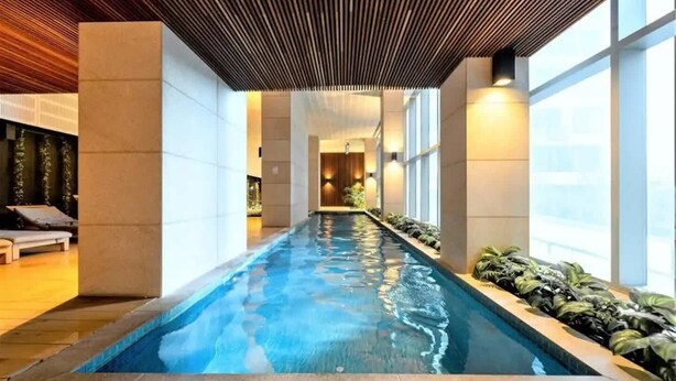Une longue piscine intérieure dotée d’un plafond en bois et de grandes fenêtres sur un de ses côtés.