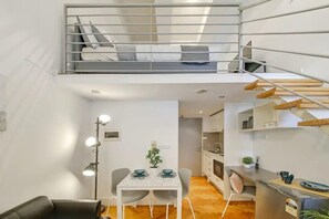 Een compact appartement met een slaapkamer op een entresol, een eethoek en een kitchenette.