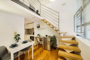 A modern apartment with a kitchen, dining area, and a wooden staircase.