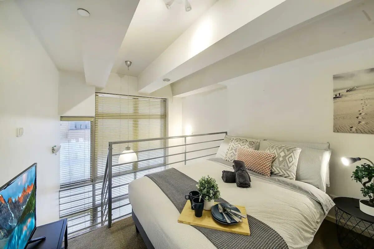 A modern bedroom with a large bed, a TV, and a balcony with a railing.