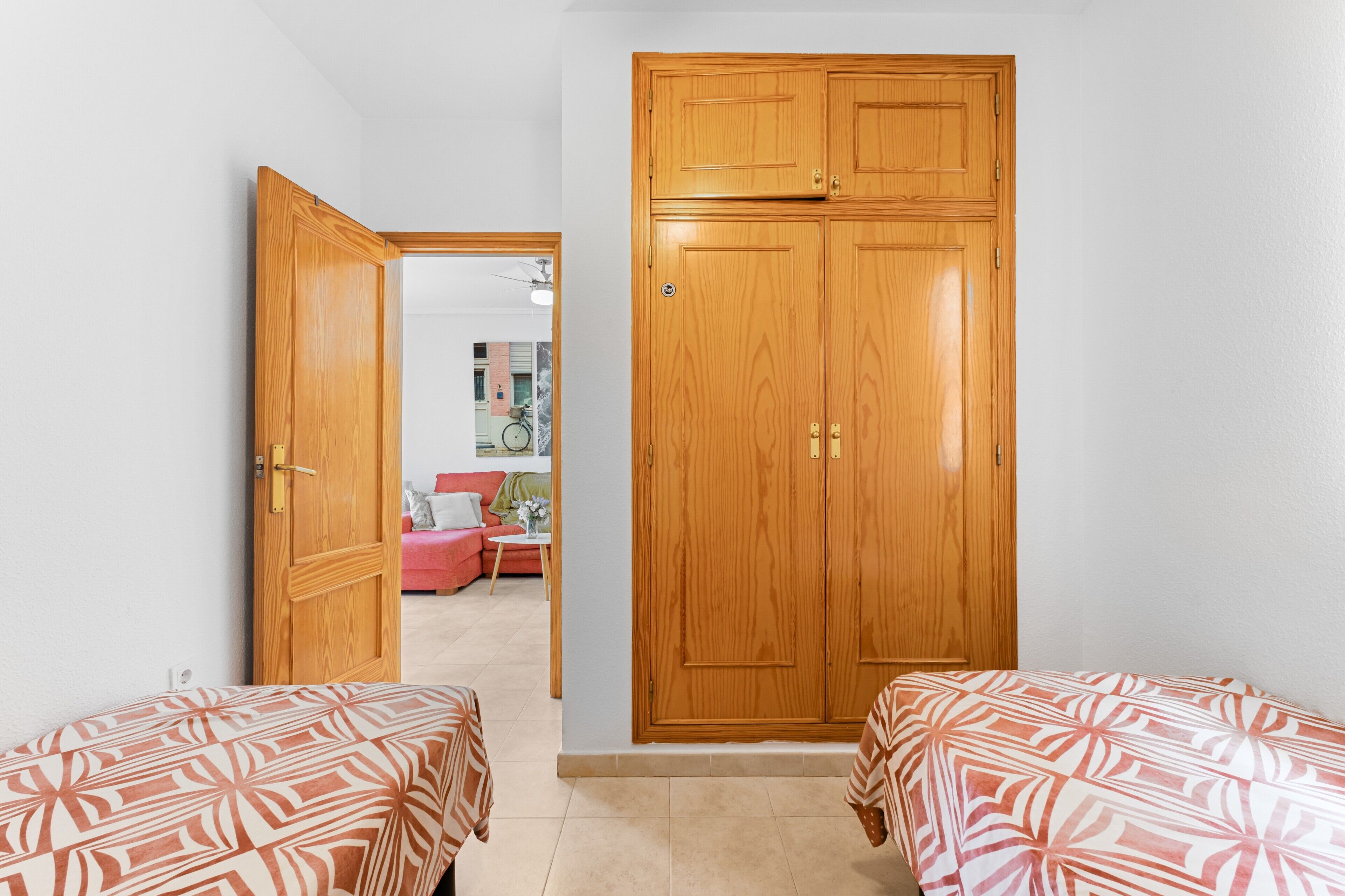 Een slaapkamer met twee bedden, een houten garderobe en een deur naar een andere kamer.