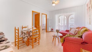 Une pièce comprenant une table à manger, des chaises, un canapé rouge, un ventilateur de plafond et une vue par la fenêtre.