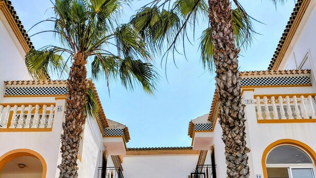 Un bâtiment doté d’une cour intérieure, de palmiers, de balcons et d’un escalier menant à un étage supérieur.