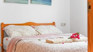 Un lit bien fait, recouvert d’une couvre-lit à motifs floraux, avec deux oreillers et un petit vase contenant des fleurs roses.