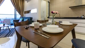A dining area with a table set for four, a kitchen in the background, and a view of the sea through large windows. - 3BR D'Pristine Suite Near LEGOLAND, Stunning Views (Nusajaya)