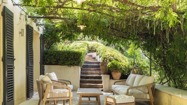 Un espace extérieur lumineux, aménagé pour se détendre, avec des meubles en osier, un escalier en béton et une végétation luxuriante.