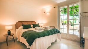 Un lit bien fait, recouvert d’une couverture verte, une lampe de chevet et une fenêtre donnant sur un paysage verdoyant.