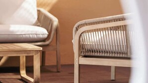 Ein Korbstuhl und ein Sofa in einem Raum mit Holzboden und einer schlichten Wand.