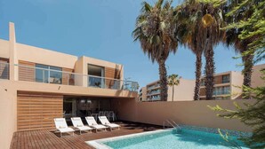 Ein modernes Hotel mit Pool auf dem Dach, Liegestühlen und Palmen.