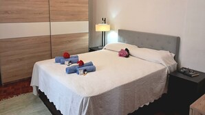 Un letto rifatto con una coperta bianca, una testiera grigia e un comodino con una lampada e un libro.