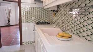 Una cucina moderna con mobili bianchi, zoccolo in piastrelle e lavello in acciaio inossidabile.