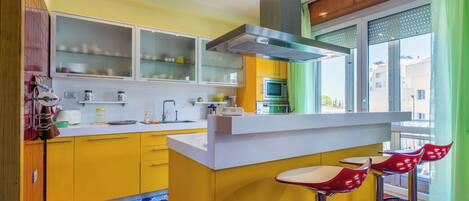 A modern kitchen with yellow cabinets, a stainless steel range hood, and a large window with green curtains.