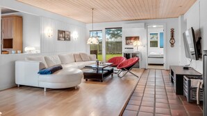 Una sala de estar moderna con un sofá blanco, sillas rojas, una mesa de centro y un televisor.