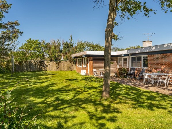 Ein Haus mit Backsteinfassade, einer Holzterrasse und einem Rasen.
