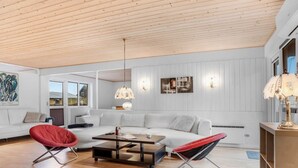 Una sala de estar moderna con un sofá blanco, sillas rojas y negras, una mesa de centro de madera y un techo con vigas de madera.