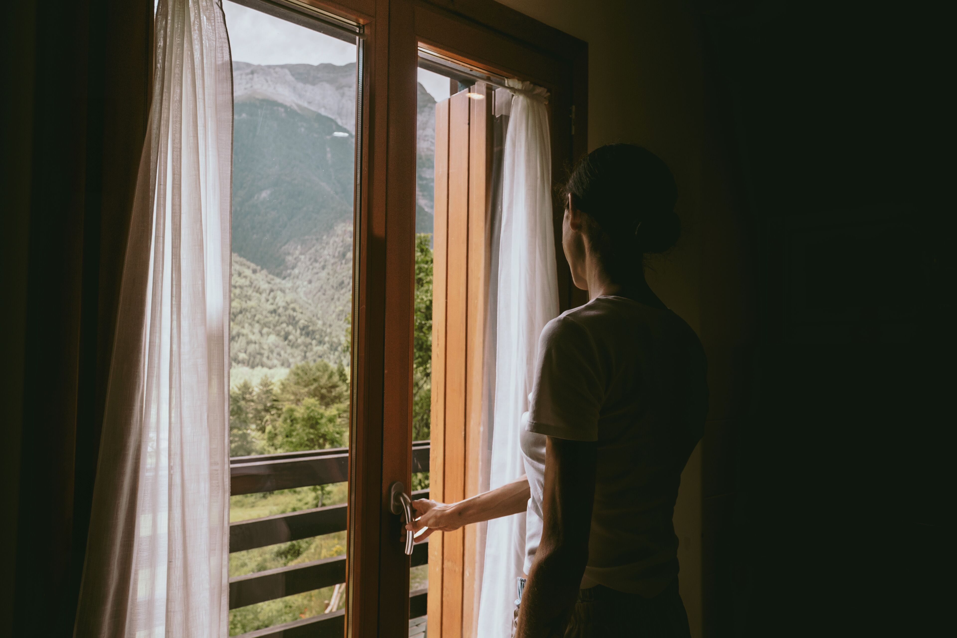 Una persona abre una puerta de madera hacia un balcón con vistas a la montaña.