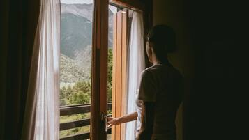 Una persona abre una puerta de madera hacia un balcón con vistas a la montaña.