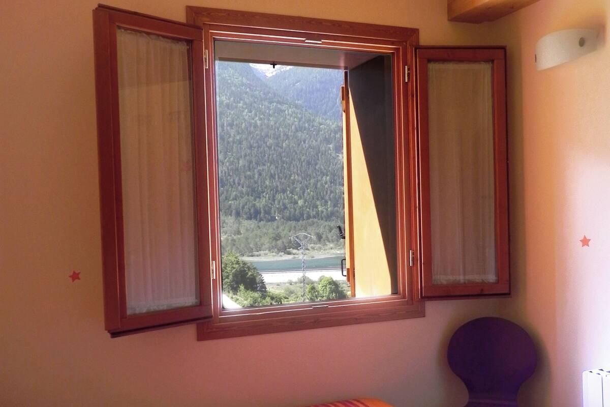 A bedroom with a bed, a chair, and a window with curtains.