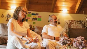 Ein gemütliches Wohnzimmer mit Holzbalkendecke, einer Couch und einer Vase mit Trockenblumen.