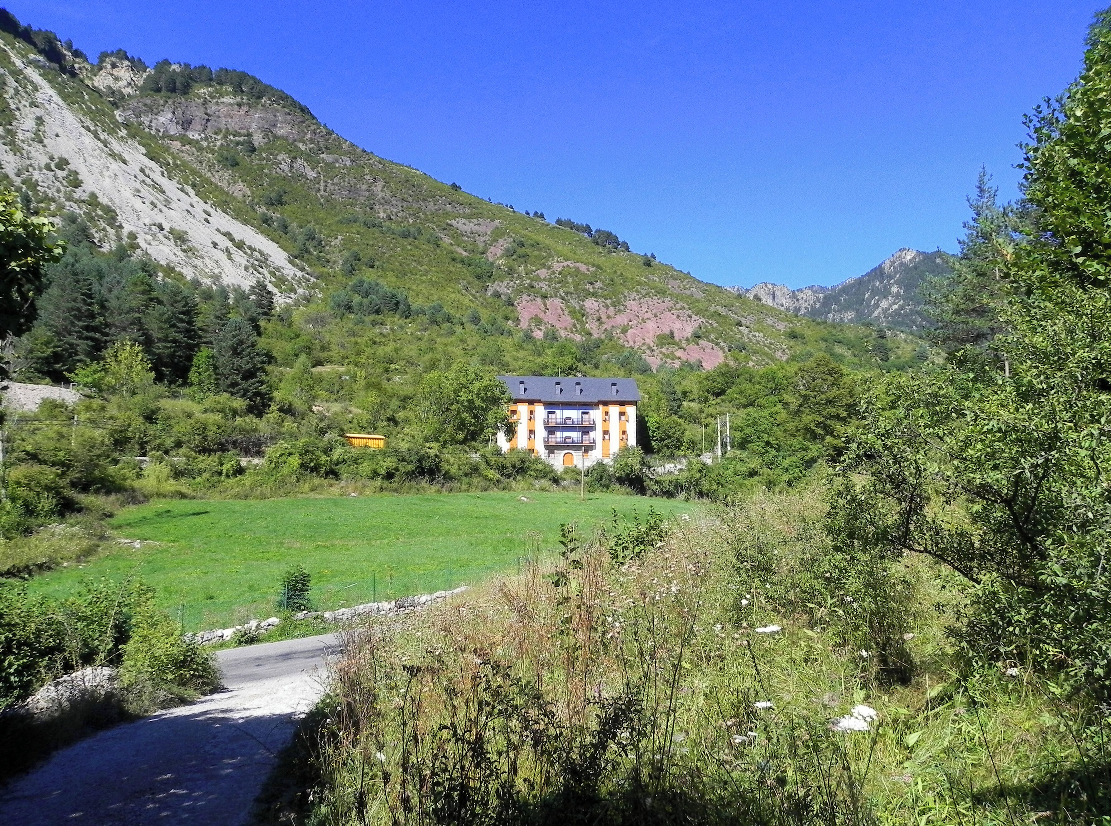 Una casa con balcón, rodeada por un campo verde y montañas.