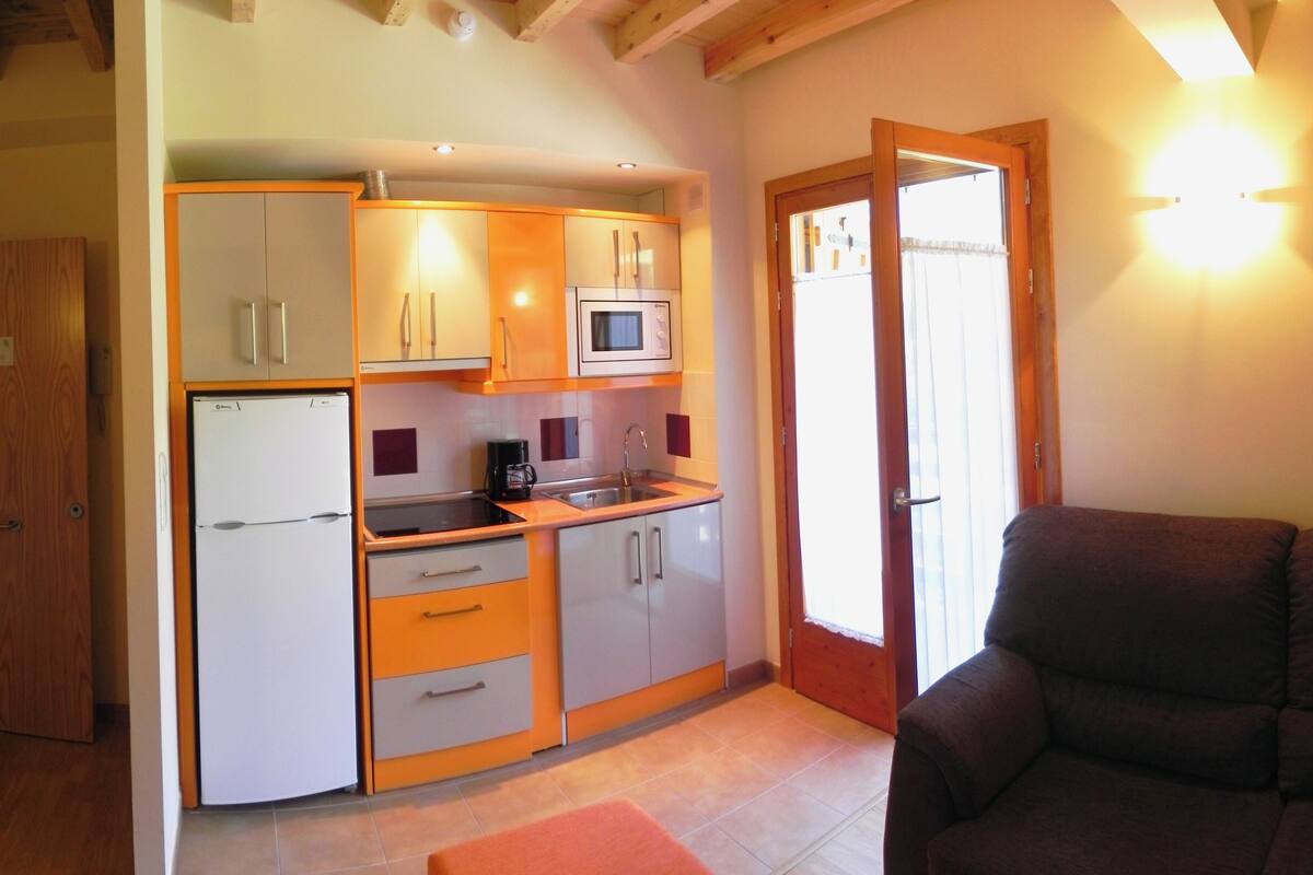 A compact kitchen with a refrigerator, microwave, and sink. There is a wooden door leading to an adjacent room.