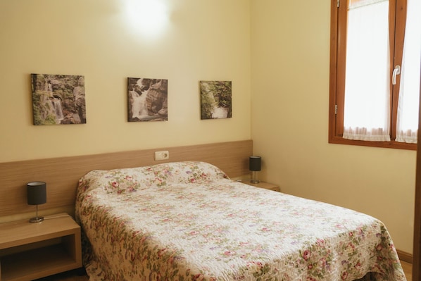 A bedroom with a bed, two bedside tables, and three wall-mounted paintings. - Caserón Baruca (Bielsa)