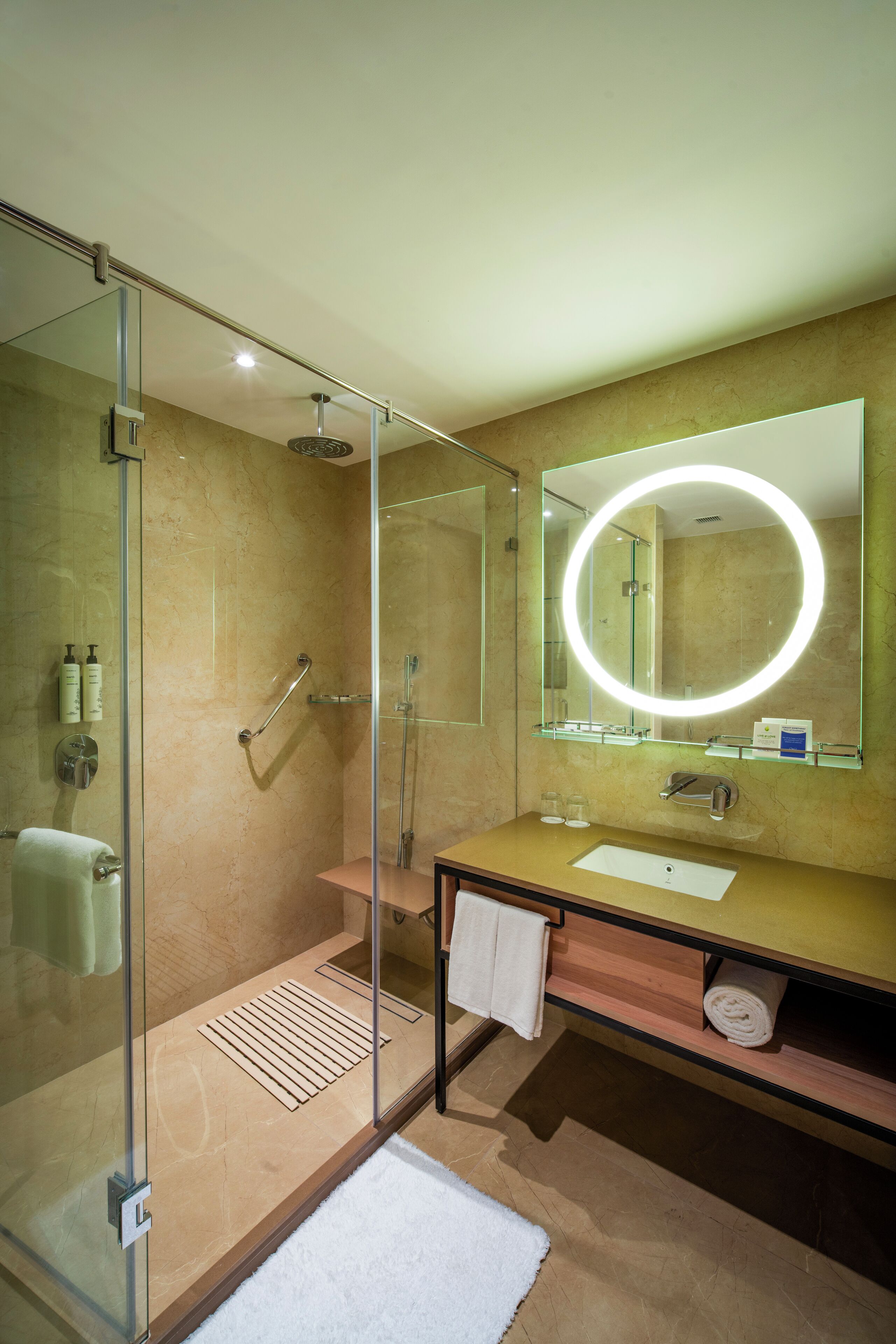 A modern bathroom with a glass-enclosed shower, a vanity with a sink, a mirror with a circular light, and a towel rack.