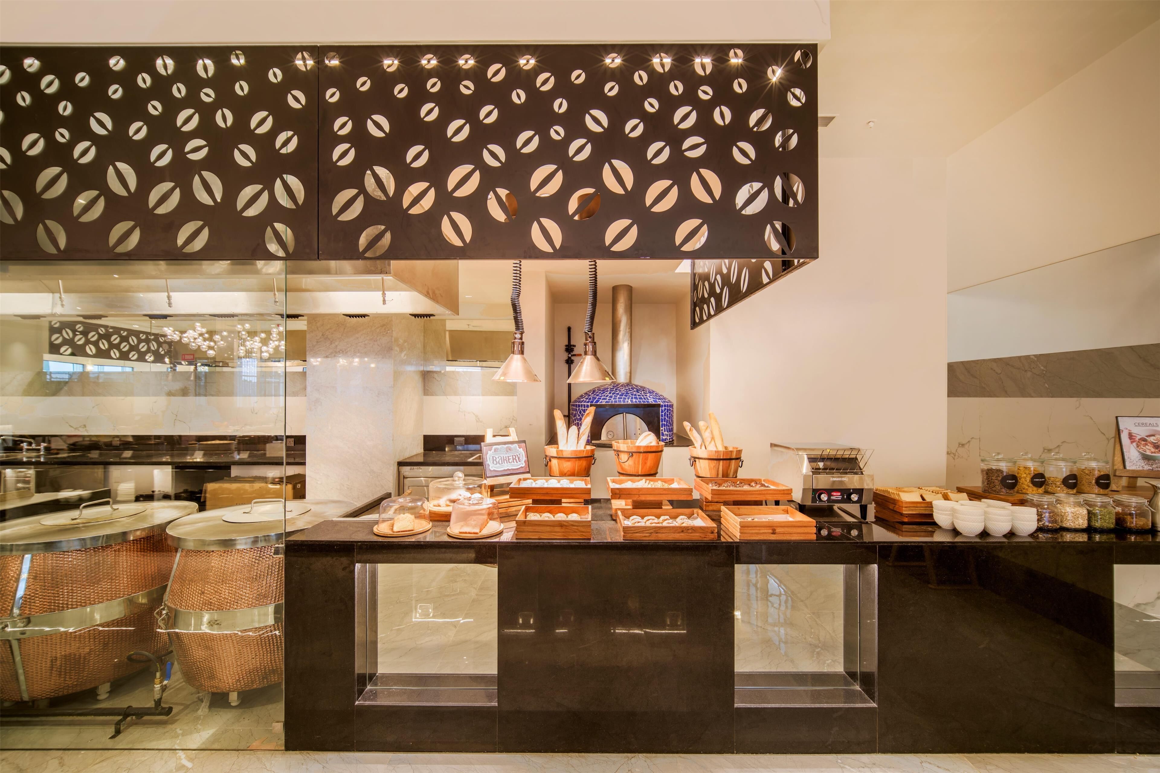 Een ontbijtbuffet met diverse soorten eten, een koffieapparaat en een decoratieve wand met een bladmotief.