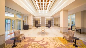 Een ruime lobby met een hoge plafond, patroonstoelen, een centrale ronde tafel en een decoratief vloerontwerp.