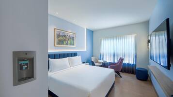 Una habitación de hotel con cama, escritorio, silla, televisor y un cuadro en la pared.