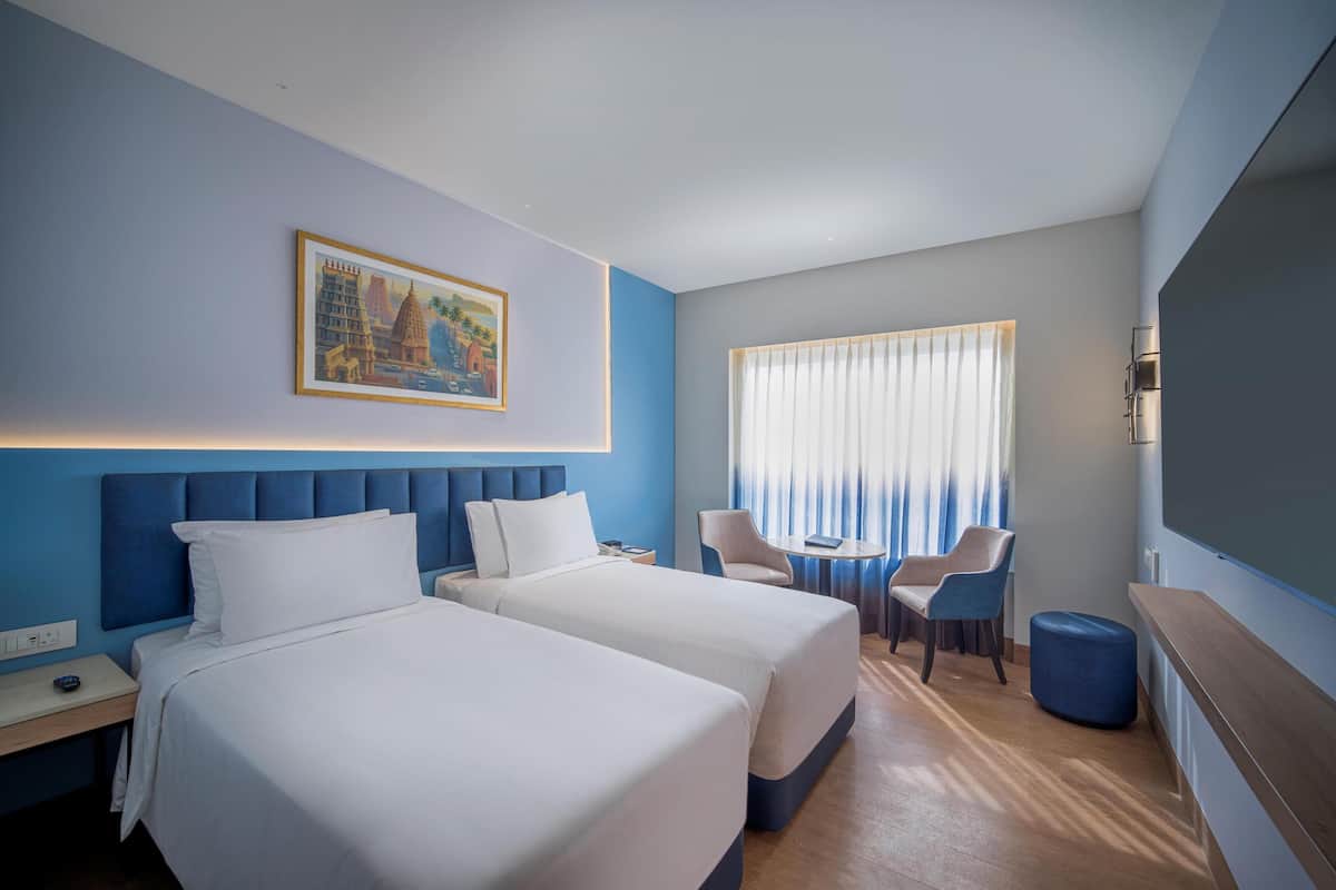 Une chambre d’hôtel avec deux lits, un bureau, une chaise, une petite table et un tableau au mur.