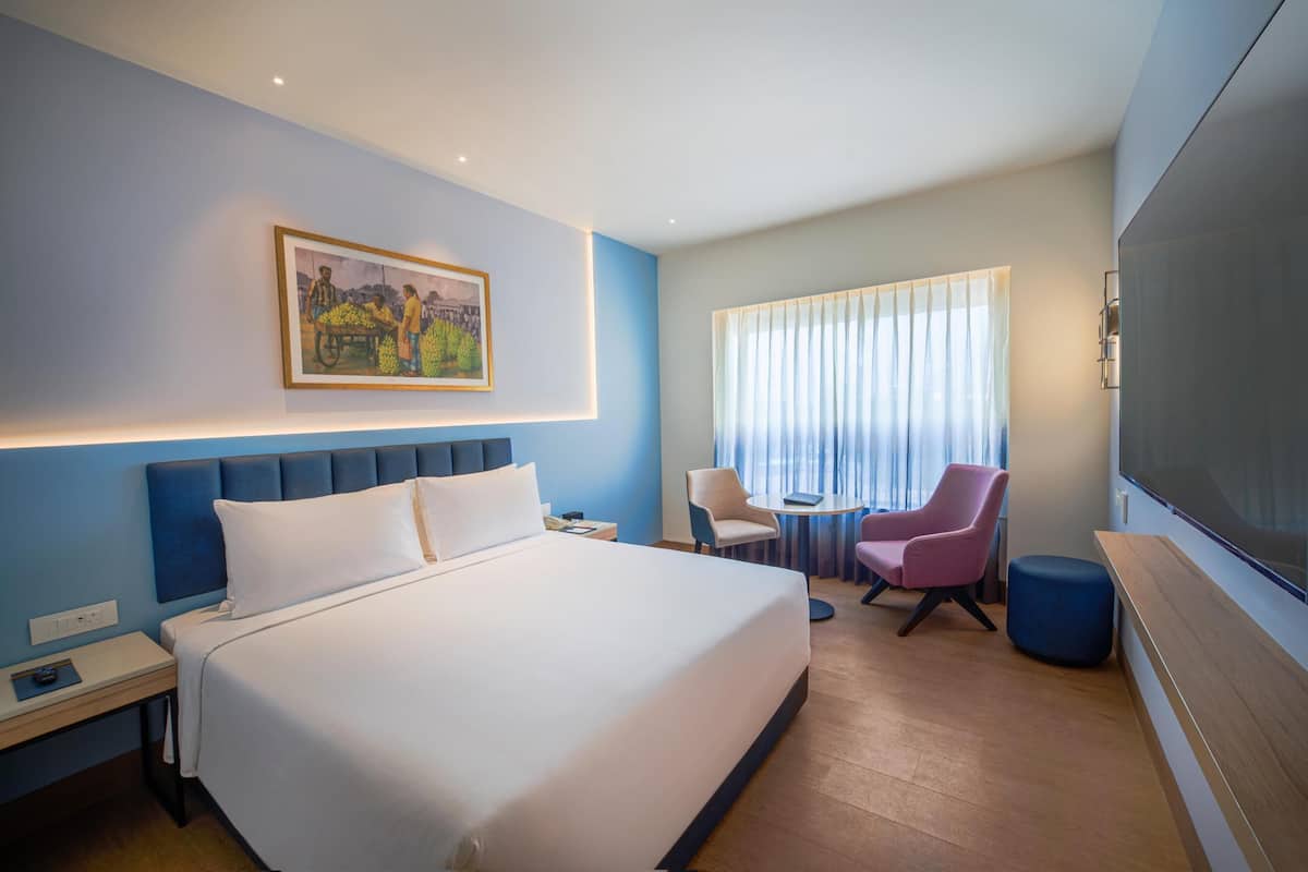 Une chambre d’hôtel avec un grand lit, un bureau, une chaise, une télévision et une fenêtre avec des rideaux.
