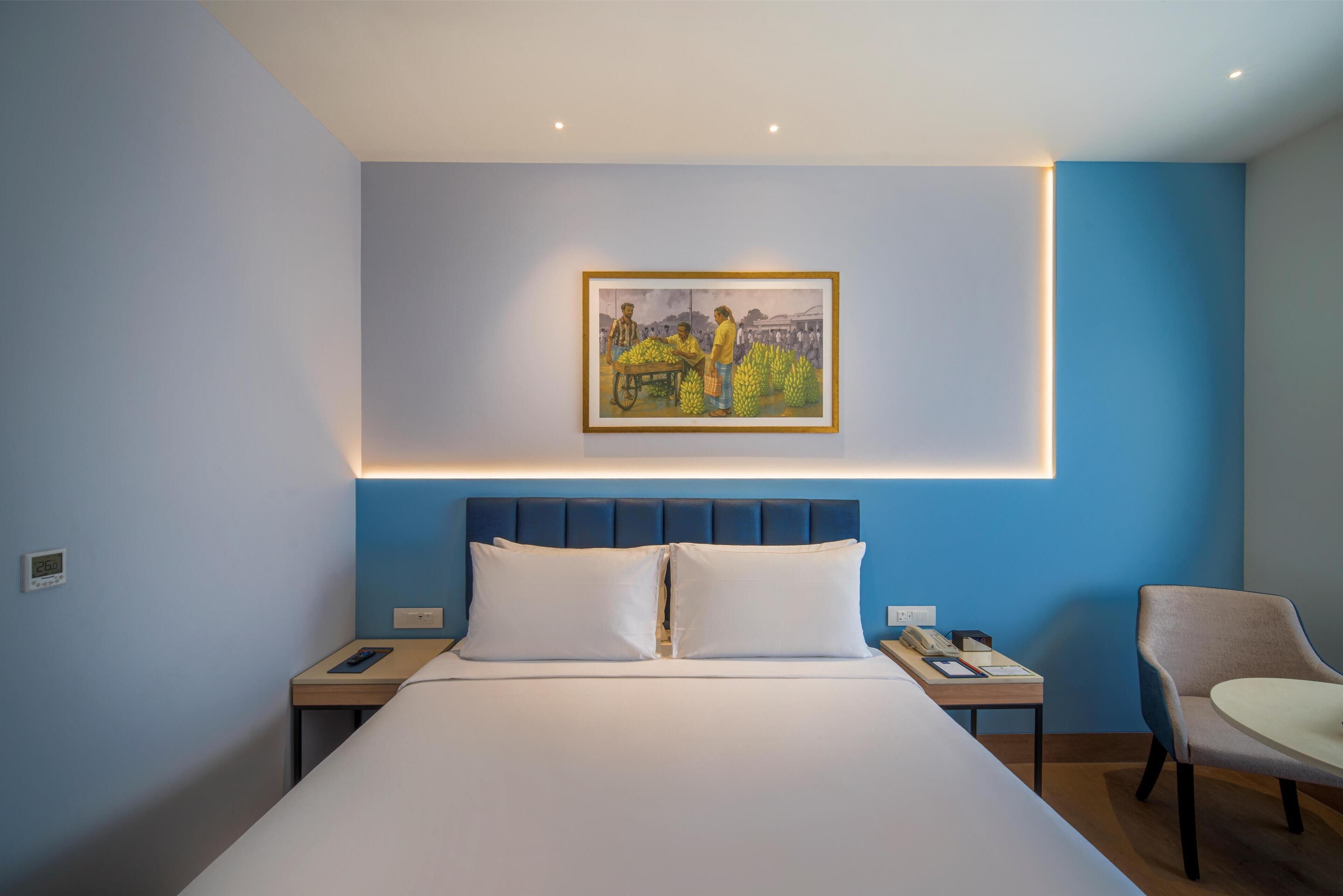 Una habitación de hotel con una cama grande, una mesita de noche con un teléfono y un libro, una silla y un cuadro en la pared.