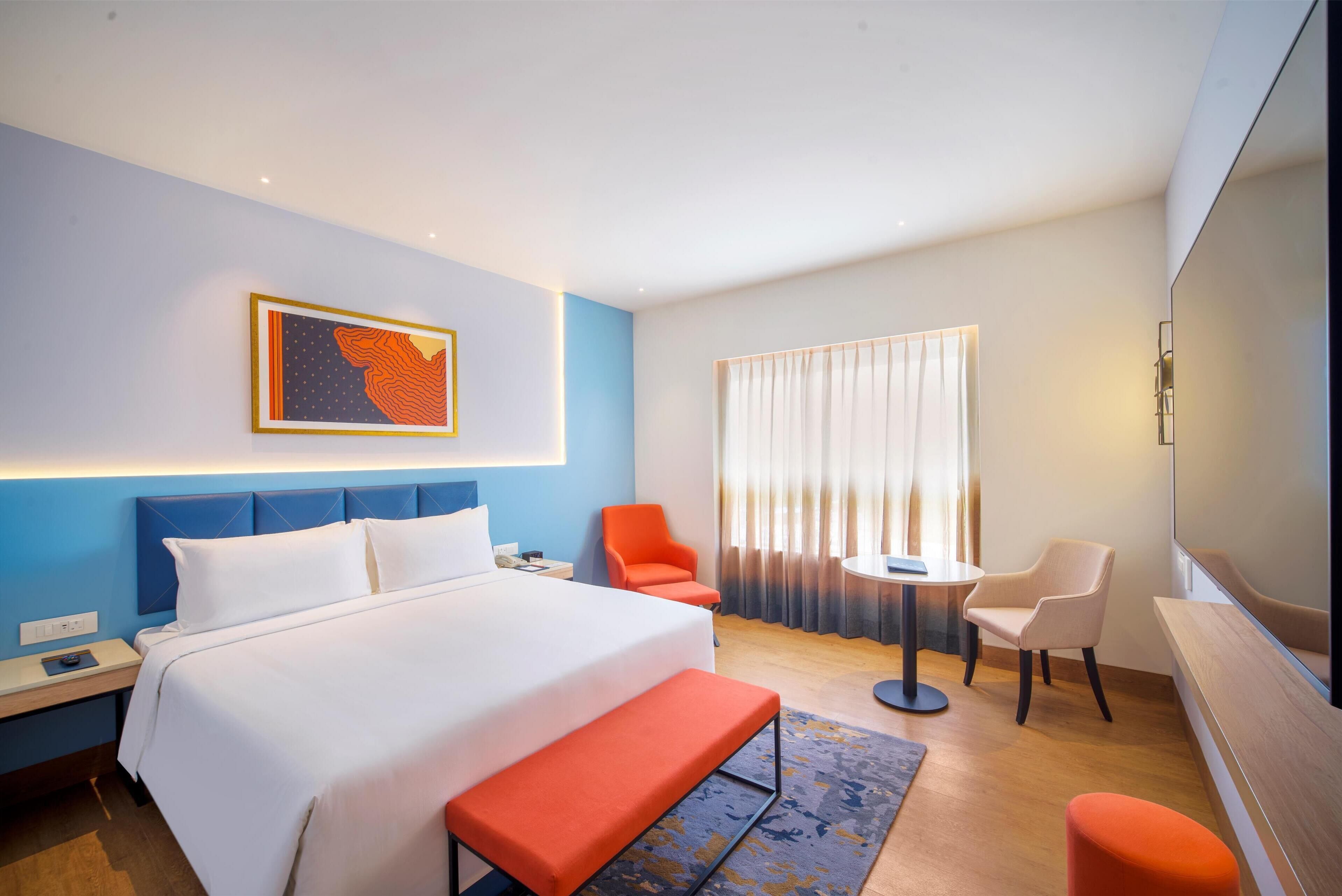 Una camera d'albergo con un letto, una scrivania, una sedia, un tavolino e un'ampia finestra con tende.