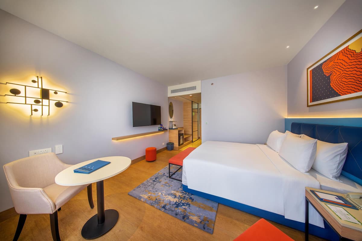 Une chambre d’hôtel avec un lit, un bureau, une chaise, une télévision et un tableau au mur.