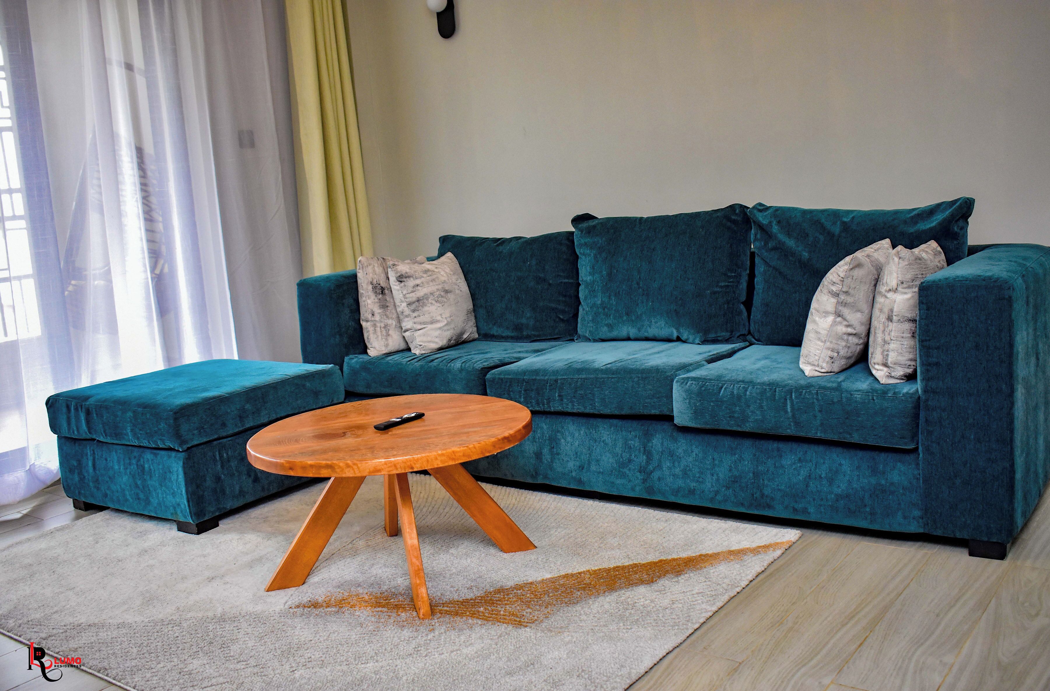 A teal sofa set with a matching ottoman, a wooden coffee table, and a light-colored rug.