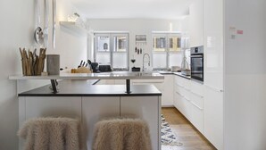A modern kitchen with white cabinets, a central island with stools, and a view of the adjacent living area. - Apartment 'Lieblingsplatz' with Mountain View, Private Terrace and Wi-Fi (Bad Tölz)