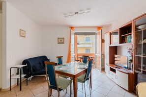 Un comedor con mesa de vidrio, sillas, sofá y estantería.