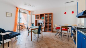 Una cocina moderna con armarios azules, un comedor con mesa y sillas, y una sala de estar con sofá y televisor.