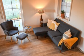 Een moderne woonkamer met een grijze bank, een zwarte fauteuil, een bijzettafeltje en een vloerlamp.