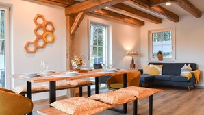 Ein Essbereich mit einem Holztisch, Bänken und Stühlen. Es gibt eine Couch mit Kissen und ein Fenster mit Aussicht.