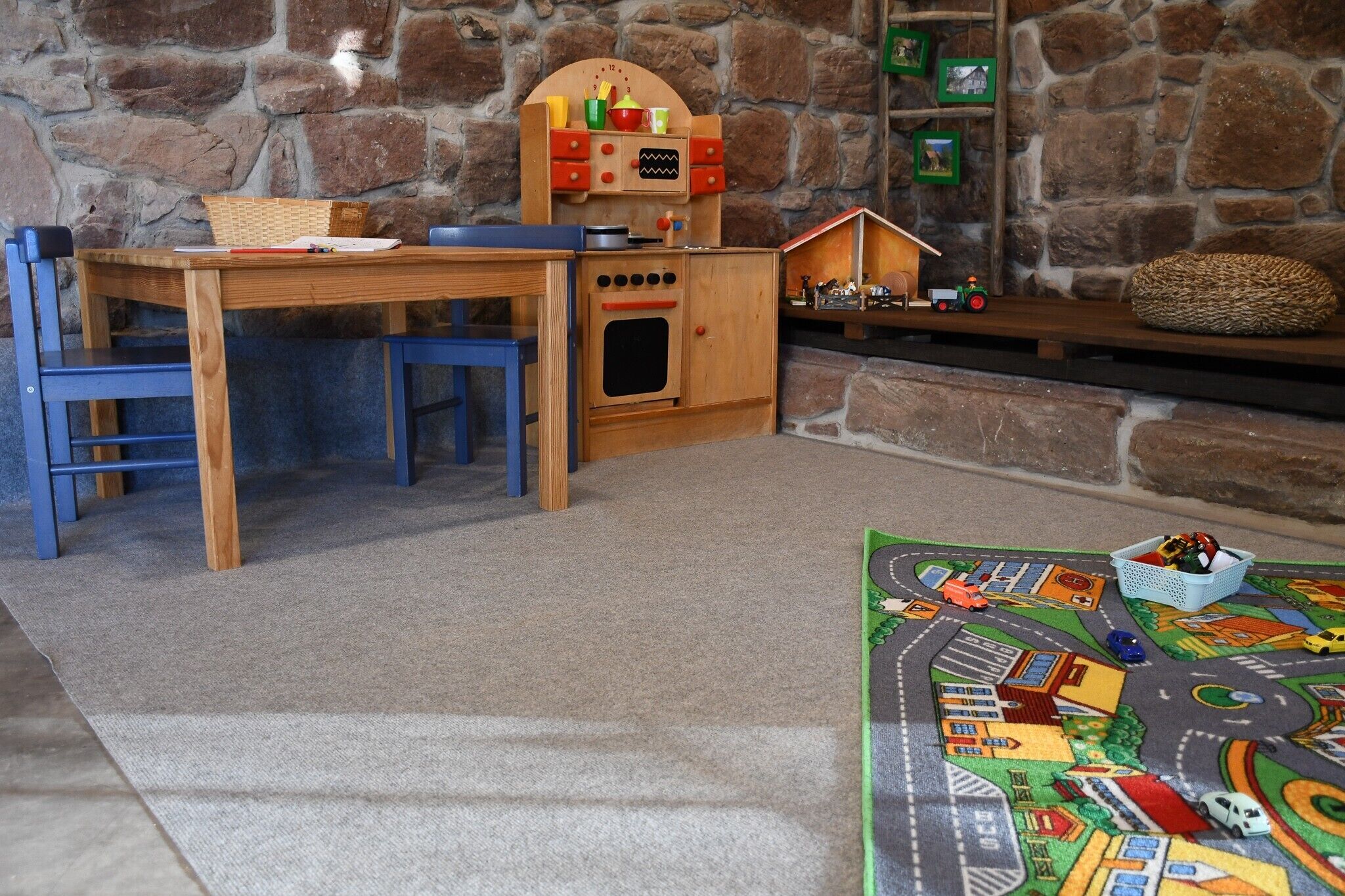A cozy room with a wooden table, chairs, a small kitchen set, a toy train set, and a play mat.