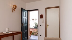 A room with a bed, a wooden table, a dark door, and a light switch on the wall. - Casa Marzia by Wonderful Italy (Olbia)